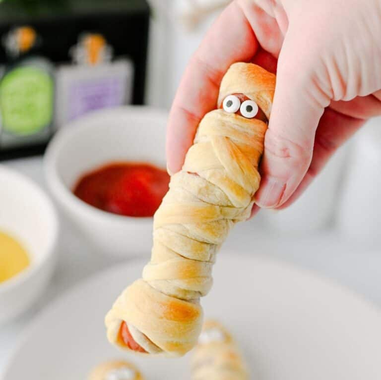 These Mummy Hot Dogs are the perfect easy Halloween dinner, spooky party snack, or kid-friendly Halloween appetizer! Made with hot dogs wrapped in flaky crescent roll dough, these adorable Crescent Roll Mummy Hot Dogs are quick to prep and baked until golden. Add candy eyes for a fun finishing touch, then serve with ketchup and mustard for dipping. If you need Easy Halloween Food Ideas, Halloween Party Food For Kids, Halloween Hot Dog Ideas, Halloween Finger Foods, Spooky Halloween Snacks, or Halloween Dinner Ideas For Kids, this simple recipe is a must-try. These Halloween Mummy Dogs are great for Halloween parties, movie nights, or a festive family dinner. Save this Mummy Hot Dogs Recipe for an easy Halloween snack that's cute, delicious, and made with a few simple ingredients!