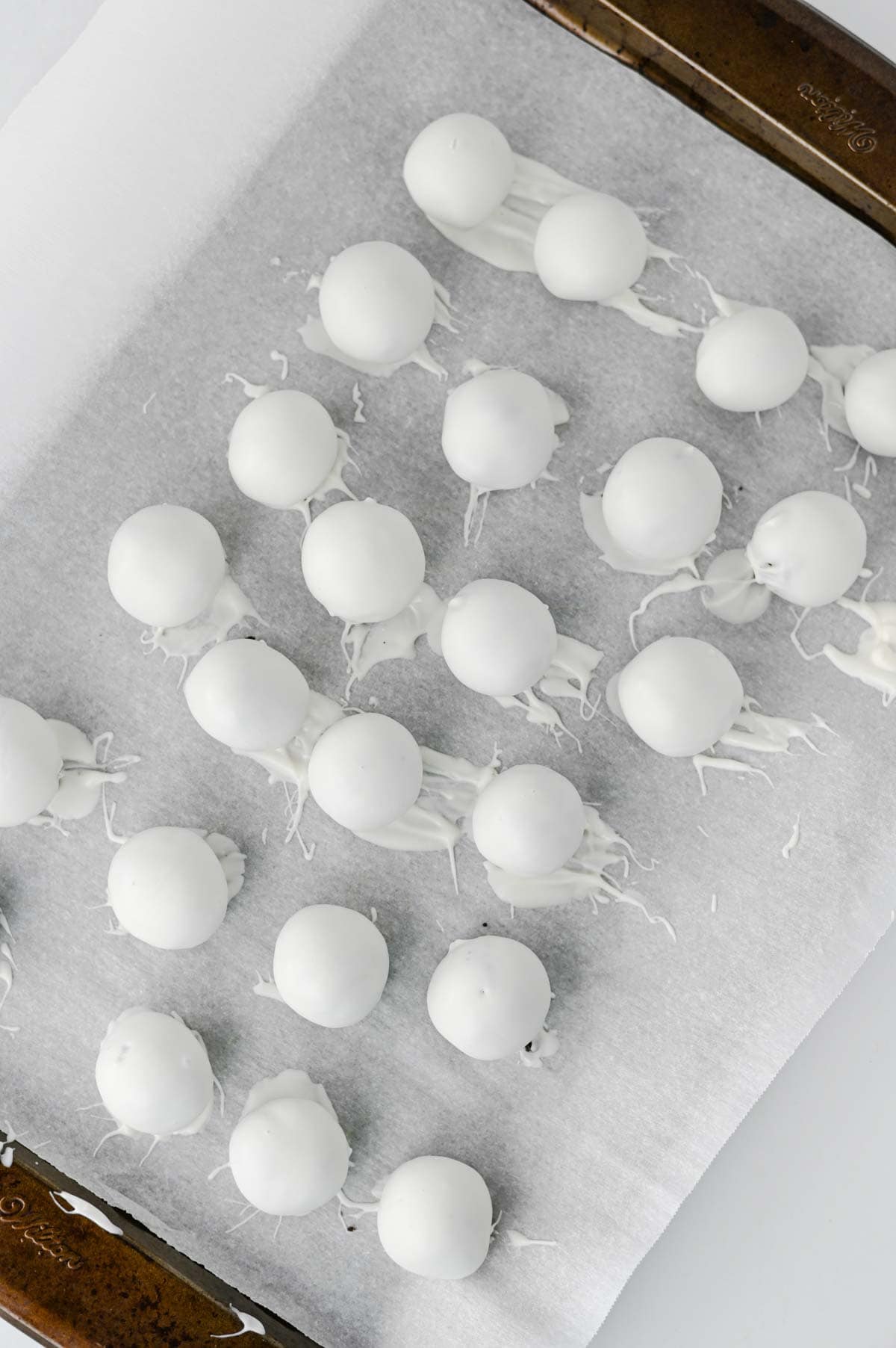 white almond bark dipped oreo balls on a parchment paper lined baking sheet