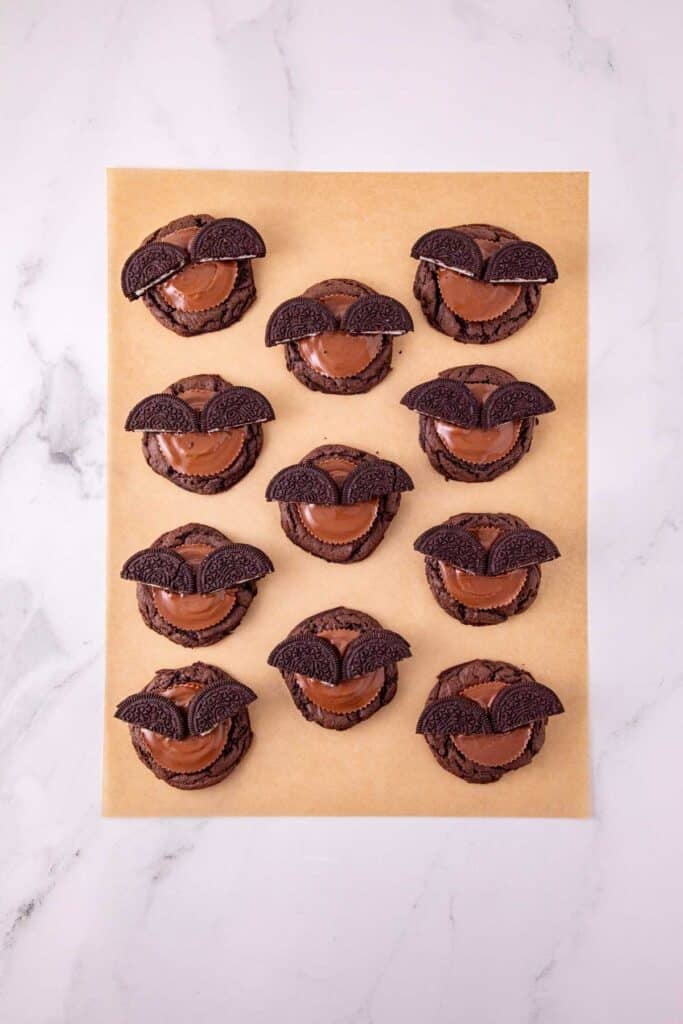 oreo halves and peanut butter cups on top of chocolate cookies on parchment paper
