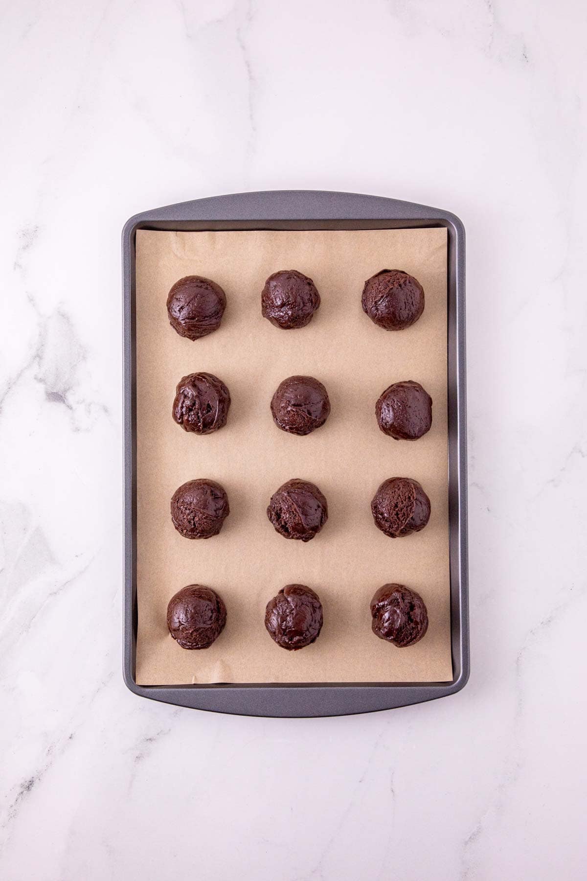 chocolate cookie dough balls on a parchment lined baking sheet