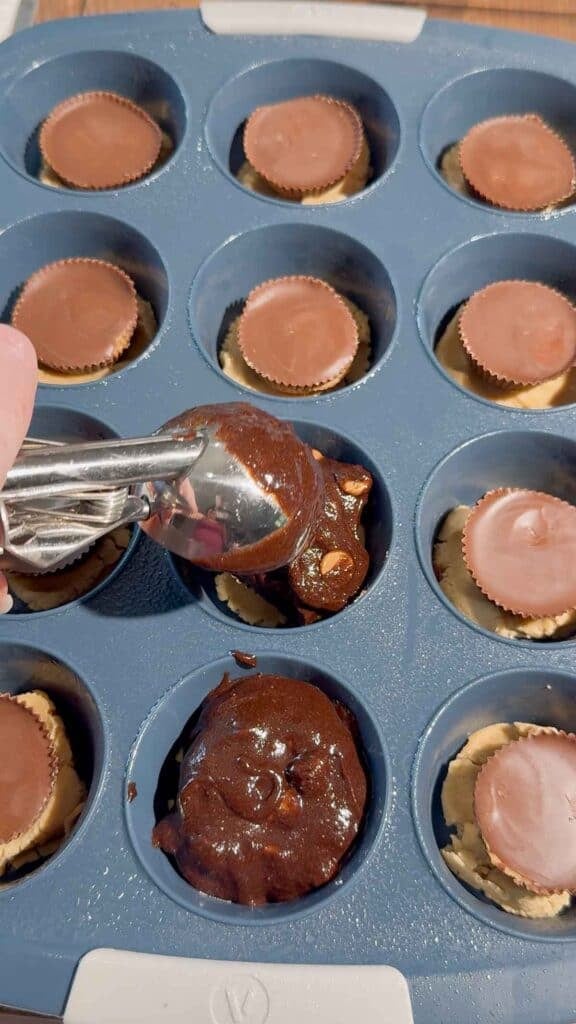 scooping brownie batter over peanut butter cups and peanut butter cookie dough in muffin tins
