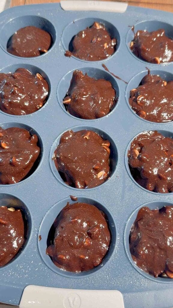 brownie batter on top of peanut butter cups and cookie dough in a muffin tin