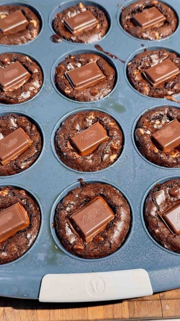 Reese's Stuffed Peanut Butter Brookies are the ultimate dessert for chocolate and peanut butter lovers! These easy muffin tin brookies start with Pillsbury peanut butter cookie dough, then get loaded with Reese's Peanut Butter Cups, Reese's brownie batter and pieces of Reese's peanut butter bar. Ready in just 33 minutes, this easy brookie recipe is perfect for parties, potlucks, holidays or whenever you need an indulgent treat. Save this recipe if you love Reese's desserts, peanut butter cup recipes, brownie cookie desserts, stuffed brookies, easy brownie mix recipes and muffin tin desserts. Every bite has a chewy peanut butter cookie base, a gooey candy center and a fudgy brownie top. These brownie cups are easy to serve and packed with chocolate peanut butter flavor!