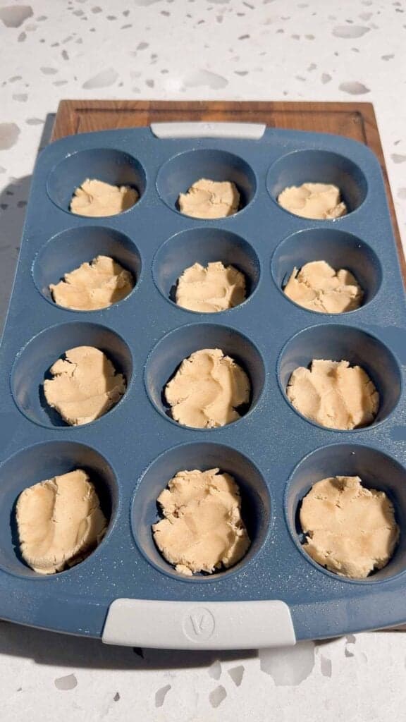 peanut butter cookie dough in the bottom of muffin tins