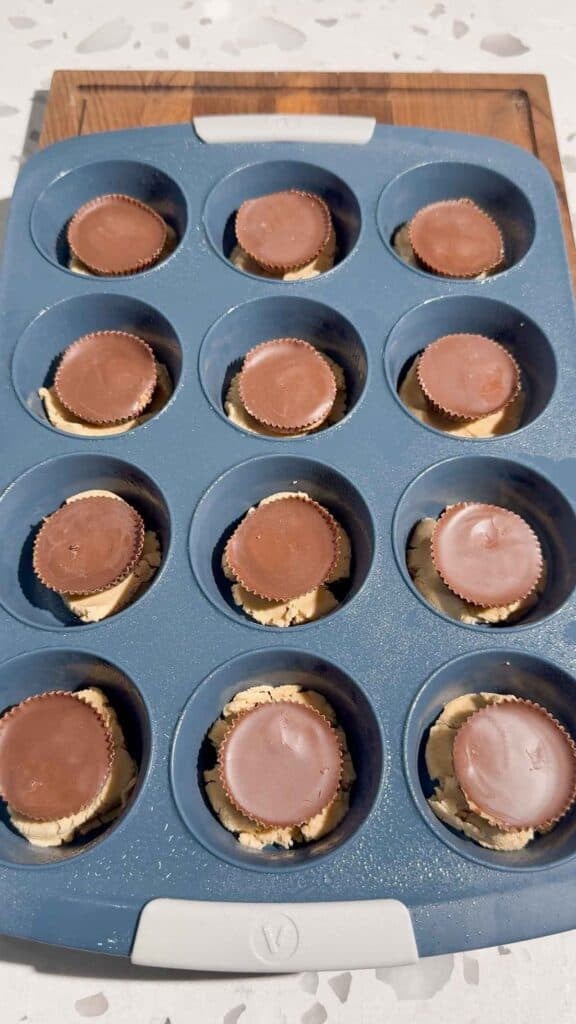 peanut butter cups on top of peanut butter cookie dough in muffin tins
