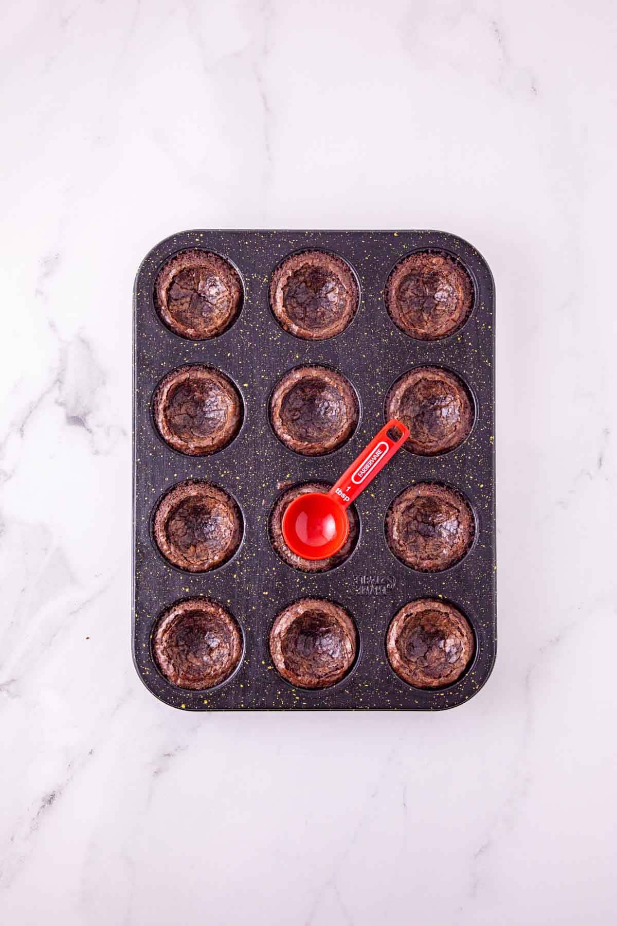 pressing a spoon into the center of mini brownies in a muffin tin
