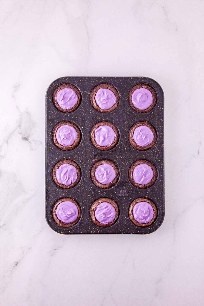 purple frosting on top of mini brownies in a muffin tin