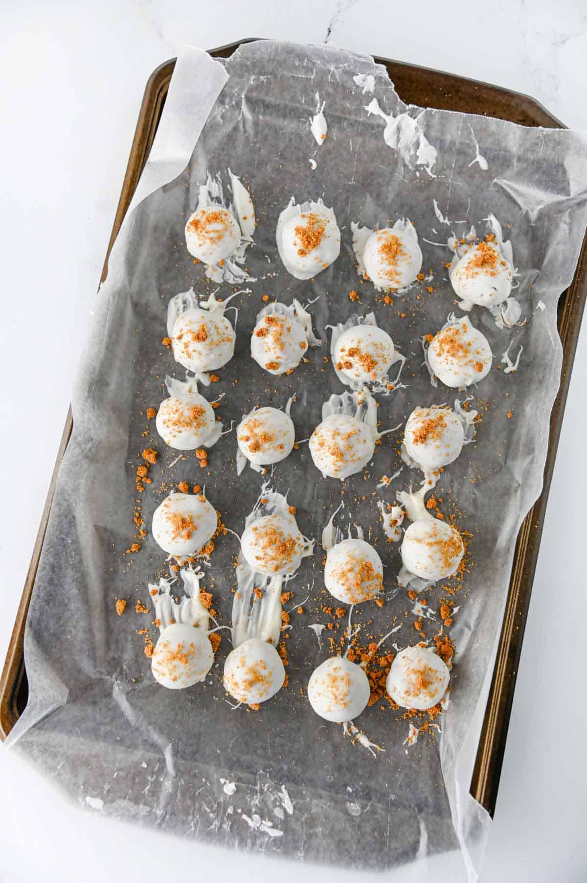 biscoff crumbs on top of almond bark dipped truffles on a baking sheet