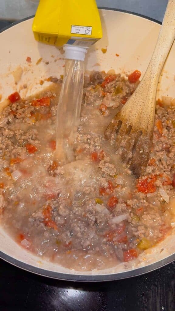 broth being added to pot with ground beef and rotel