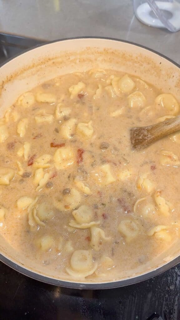 stirring ground beef tortellini soup in a pot