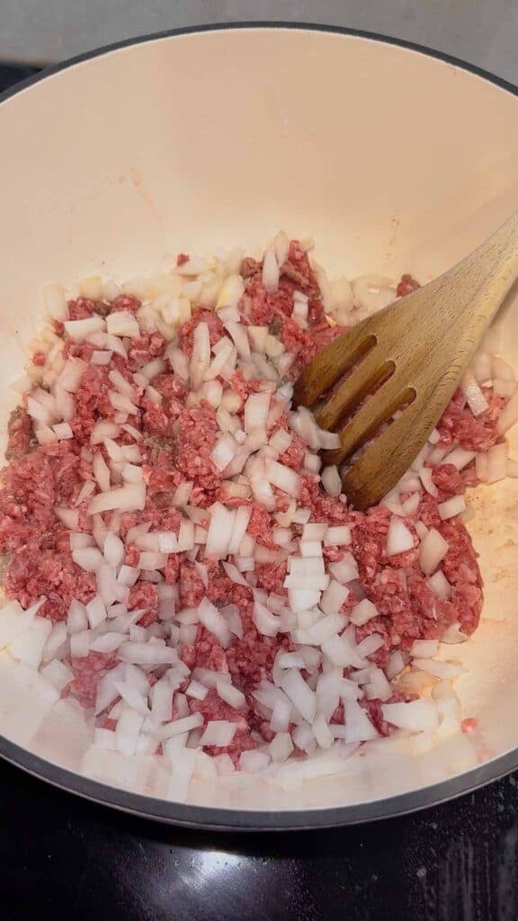 diced onions on top of ground beef in a dutch oven