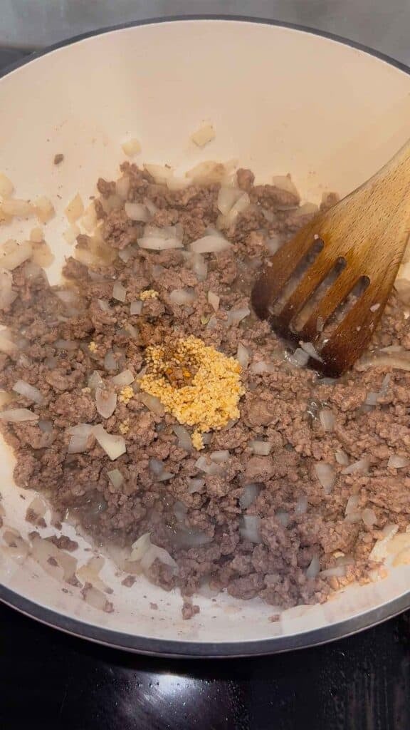 chopped garlic on top of ground beef and onions in a dutch oven