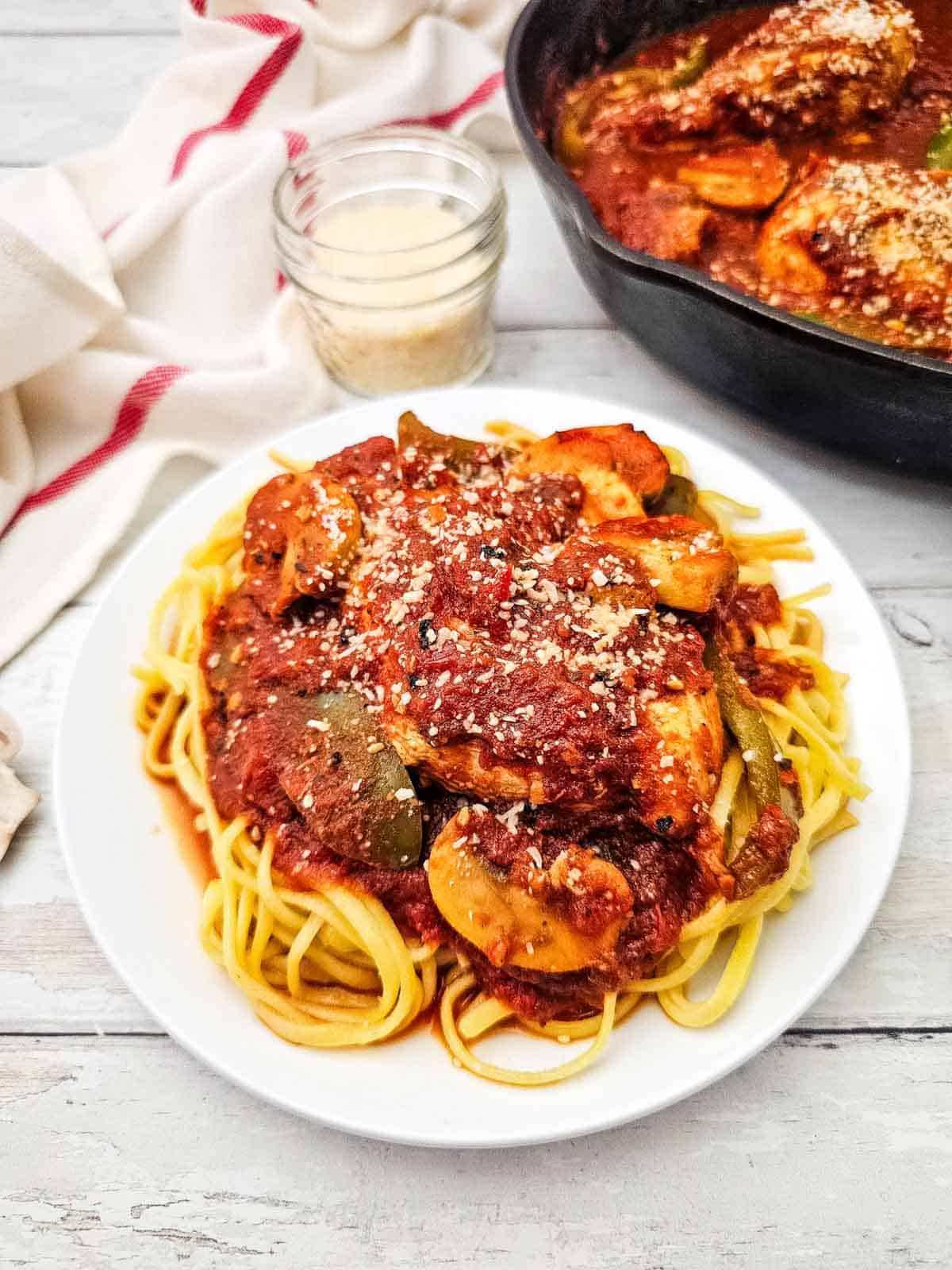 chicken cacciatore on top of noodles on a plate