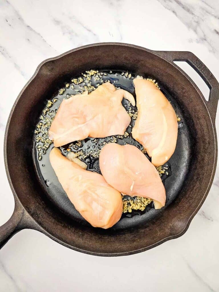 Sautéed chicken breast in skillet with garlic and herbs.