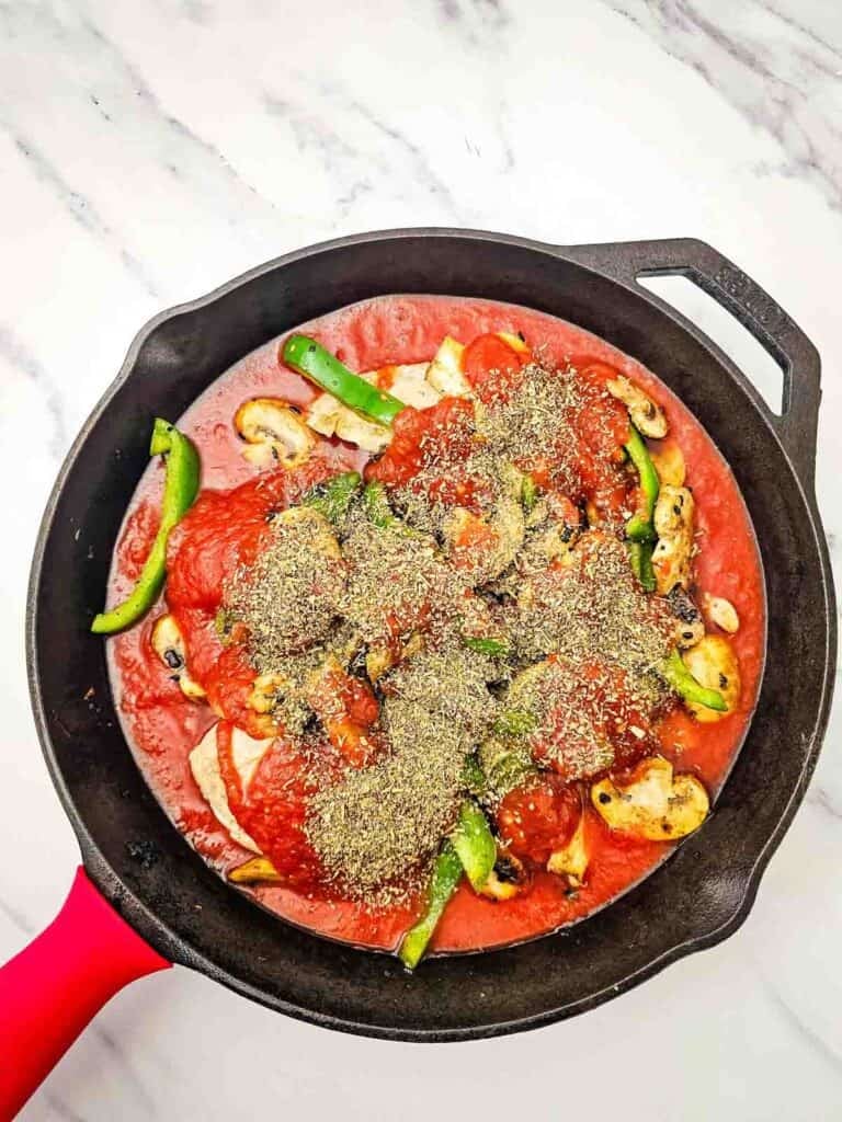 seasoning on top of chicken breasts in tomato sauce in a skillet