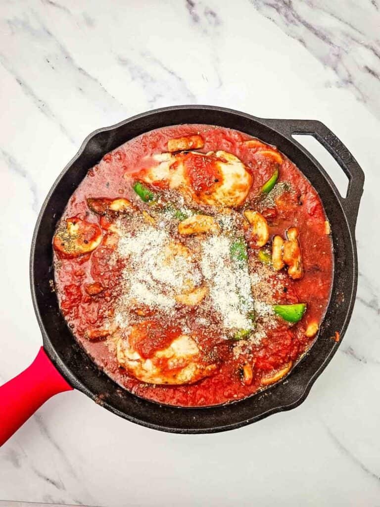 grated parmesan on top of chicken breasts in a tomato sauce in a skillet