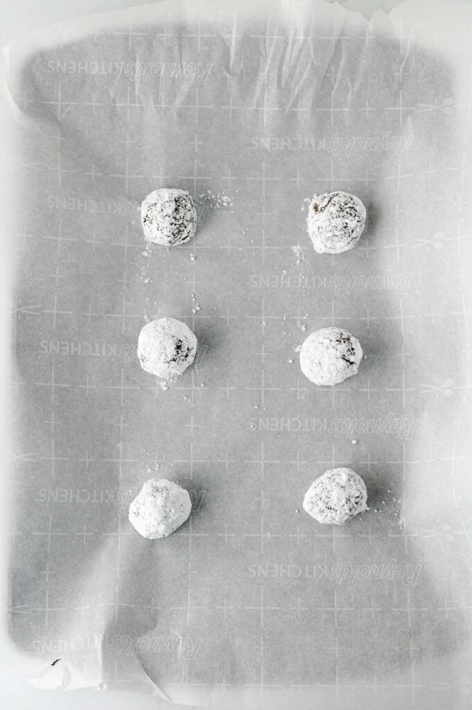 powdered sugar coated cookie dough balls on a parchment lned baking sheet
