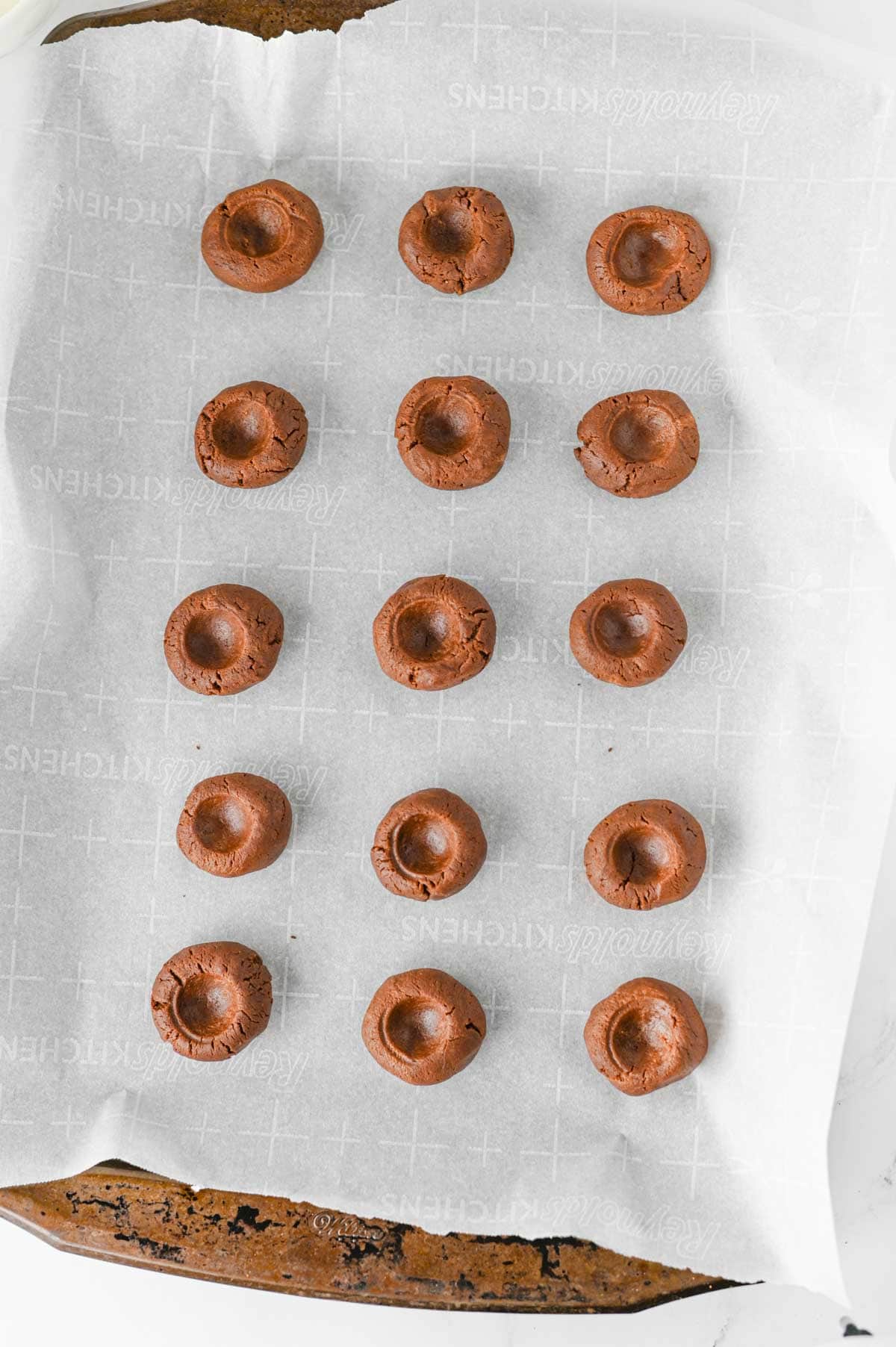 indents in balls of chocolate cookies dough on a parchment lined baking sheet