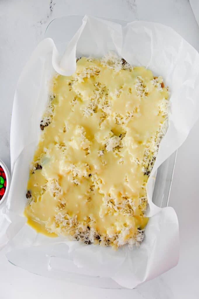 condensed milk poured over coconut cookie bars in baking dish