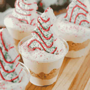 Christmas Tree Cake Dirt Cups are an easy no bake Christmas dessert made with Little Debbie Christmas Tree Cakes, Golden Oreos, creamy vanilla pudding and fluffy Cool Whip! These festive Christmas dessert cups are layered with crushed cookies and pudding, then topped with red and green sanding sugar and a Christmas Tree Cake. Ready in just 15 minutes, this simple holiday dessert recipe is perfect for Christmas parties, holiday potlucks, classroom celebrations and family gatherings. If you're looking for easy Christmas desserts, individual holiday treats, no bake dessert cups or fun Christmas recipes for kids, these Christmas Tree Cake pudding cups are a delicious choice. Save this quick Christmas dessert idea for your holiday dessert table!