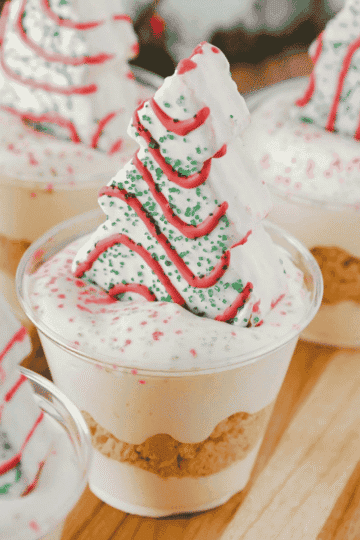 Christmas Tree Cake Dirt Cups are an easy no bake Christmas dessert made with Little Debbie Christmas Tree Cakes, Golden Oreos, creamy vanilla pudding and fluffy Cool Whip! These festive Christmas dessert cups are layered with crushed cookies and pudding, then topped with red and green sanding sugar and a Christmas Tree Cake. Ready in just 15 minutes, this simple holiday dessert recipe is perfect for Christmas parties, holiday potlucks, classroom celebrations and family gatherings. If you're looking for easy Christmas desserts, individual holiday treats, no bake dessert cups or fun Christmas recipes for kids, these Christmas Tree Cake pudding cups are a delicious choice. Save this quick Christmas dessert idea for your holiday dessert table!