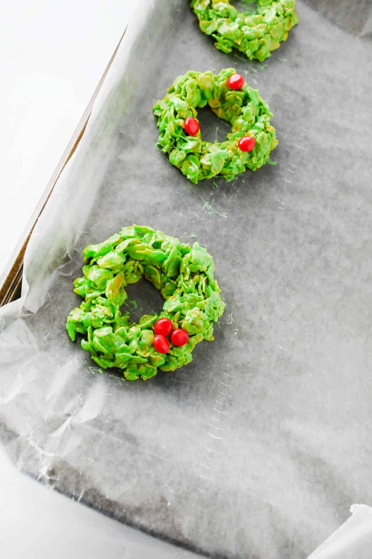 red hot candies on top of cornflake wreaths on a parchment lined baking sheet