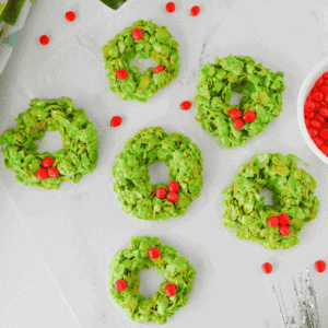 These easy Cornflake Wreaths are a fun, festive no bake Christmas dessert made with just 5 simple ingredients! Crunchy corn flakes are coated in a gooey mixture of melted marshmallows, butter and green food coloring, then shaped into adorable Christmas wreath cookies and decorated with red hot candies. This old fashioned Cornflake Wreaths recipe is perfect for Christmas cookie trays, holiday parties, classroom treats and Christmas baking with kids. If you love easy Christmas desserts, no bake Christmas cookies, marshmallow cereal treats and nostalgic holiday recipes, these cute green Christmas wreath treats belong on your holiday baking list. Make these simple Christmas cornflake cookies for a festive dessert everyone will love this season!