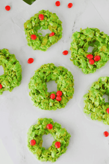 These easy Cornflake Wreaths are a fun, festive no bake Christmas dessert made with just 5 simple ingredients! Crunchy corn flakes are coated in a gooey mixture of melted marshmallows, butter and green food coloring, then shaped into adorable Christmas wreath cookies and decorated with red hot candies. This old fashioned Cornflake Wreaths recipe is perfect for Christmas cookie trays, holiday parties, classroom treats and Christmas baking with kids. If you love easy Christmas desserts, no bake Christmas cookies, marshmallow cereal treats and nostalgic holiday recipes, these cute green Christmas wreath treats belong on your holiday baking list. Make these simple Christmas cornflake cookies for a festive dessert everyone will love this season!
