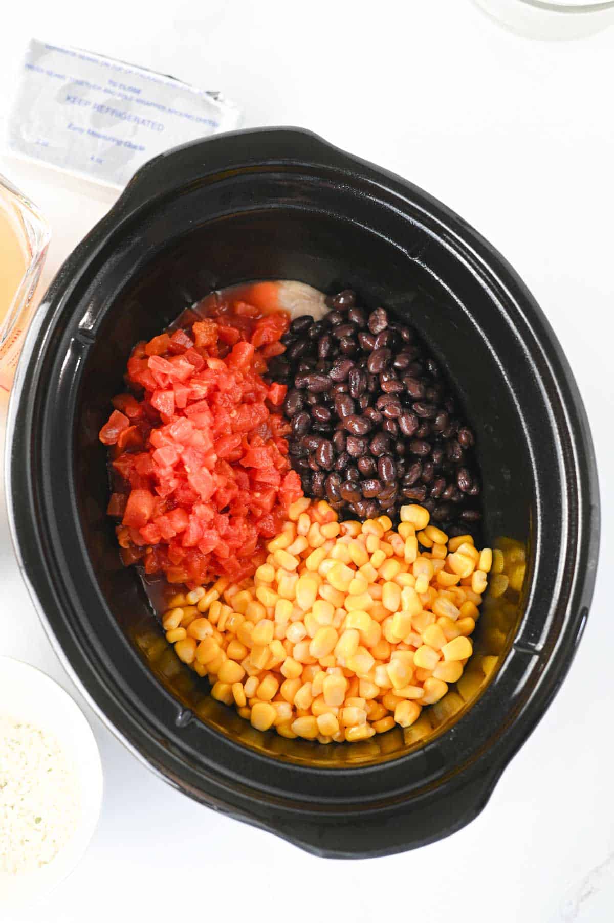 tomatoes, beans and corn on top of chicken in a crock pot