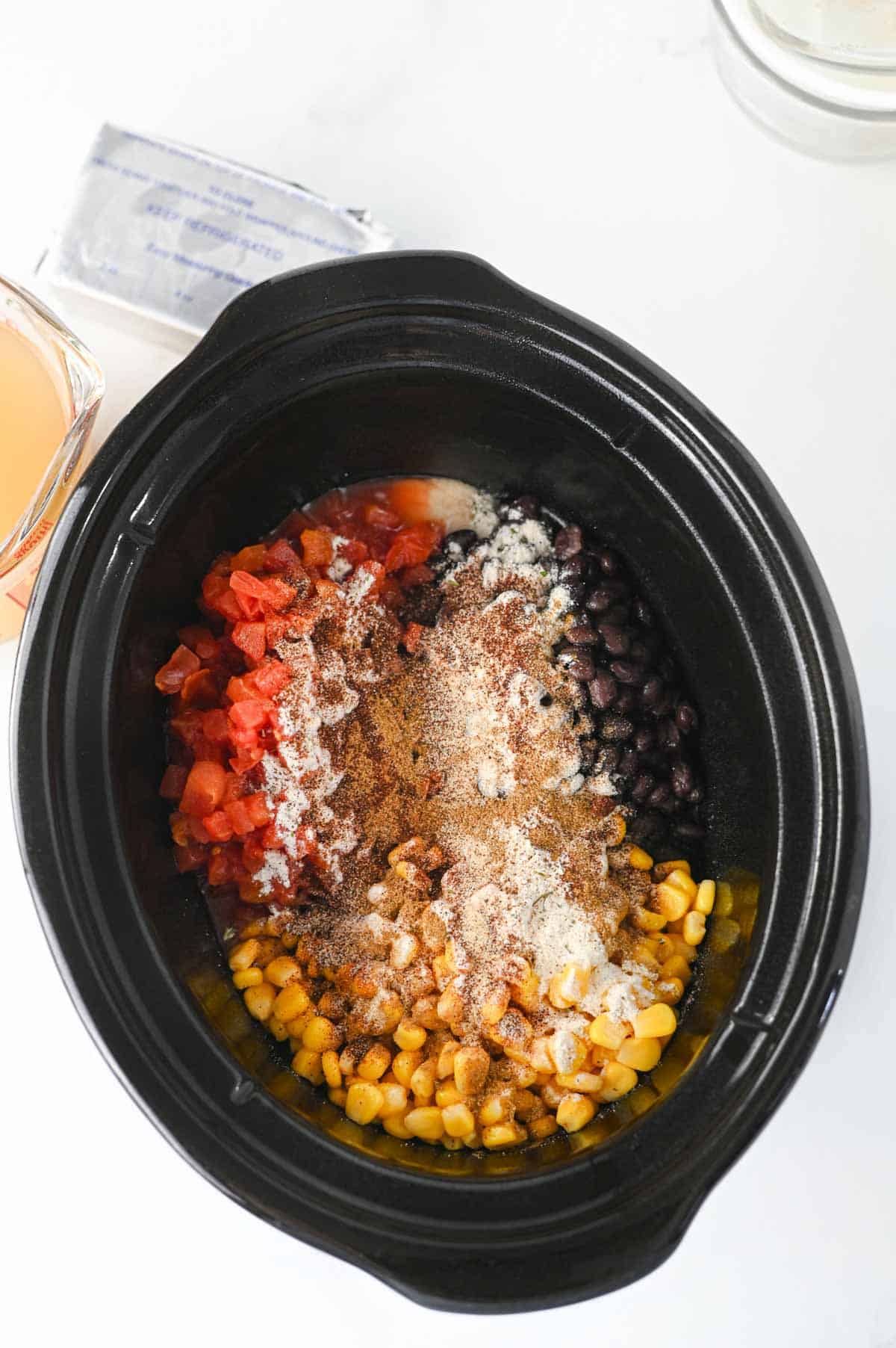 spices, tomatoes, beans and corn in a crock pot