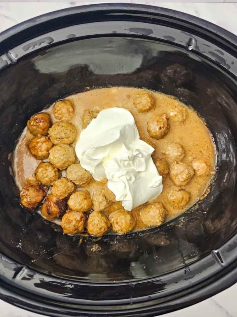 sour cream added to swedish meatballs in a slow cooker