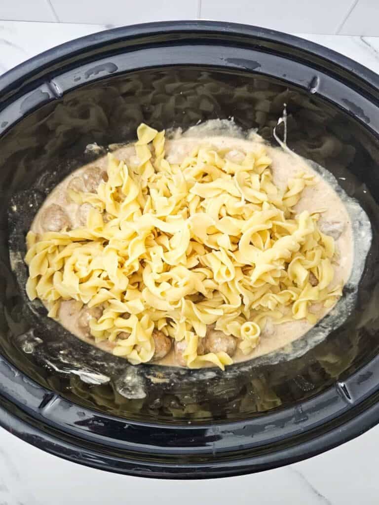 cooked egg noodles added to slow cooker with swedish meatballs