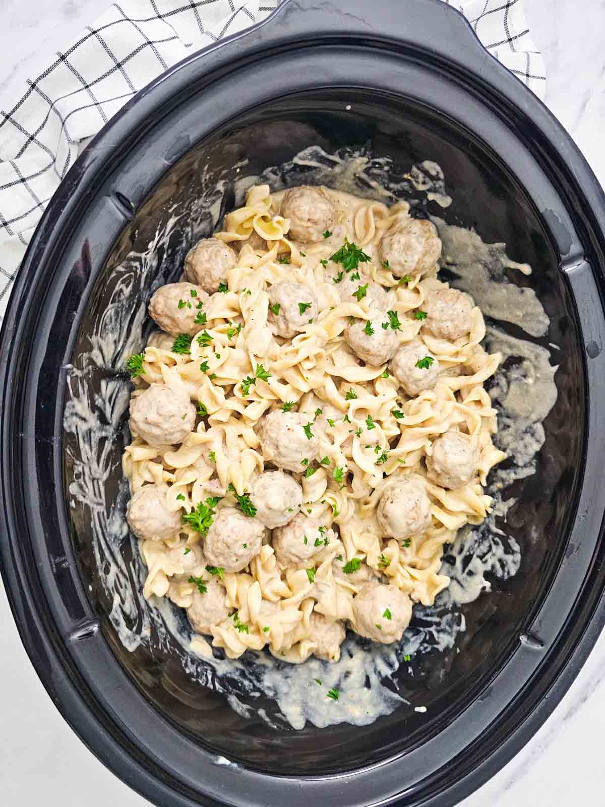 parsley on top of swedish meatballs and noodles in a slow cooker