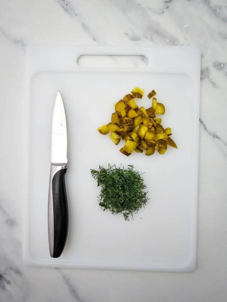 chopped dill and chopped pickles on a cutting board