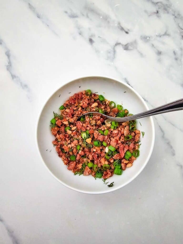 mixture of crumbled bacon, green onions and dill on a plate