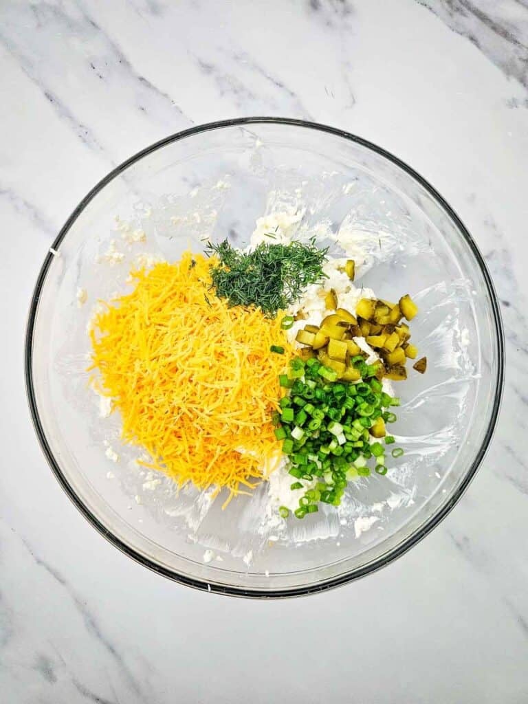 green onions, chopped pickles, chopped dill and shredded cheddar in a bowl with cream cheese