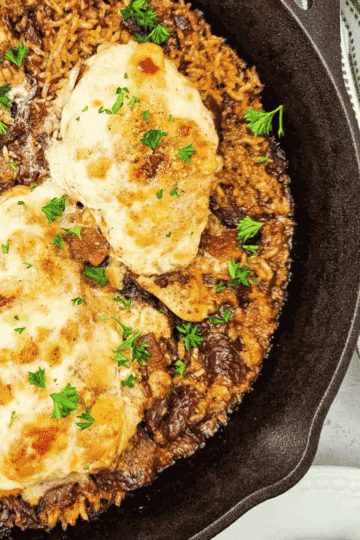 This Skillet French Onion Chicken and Rice is an easy one-pan dinner packed with cozy comfort food flavor. Tender chicken breasts bake over fluffy long grain rice in a rich mixture of French onion soup, beef consomme and butter, then get topped with creamy onion soup sour cream, crunchy croutons and melty Provolone cheese. This hearty chicken and rice skillet is perfect for busy weeknights, family dinners, cold weather meals and simple oven baked chicken recipes. If you love French onion chicken, cheesy chicken and rice, baked chicken breast recipes, skillet dinners, one pan chicken recipes and easy comfort food casseroles, this savory dinner belongs on your meal plan. A rich, satisfying recipe with minimal prep and big flavor.