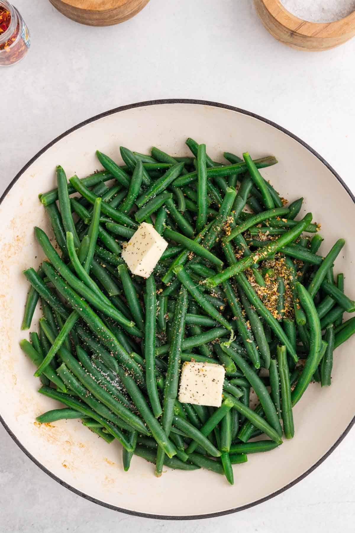 butter and italian seasoning on top of green beans in a skillet