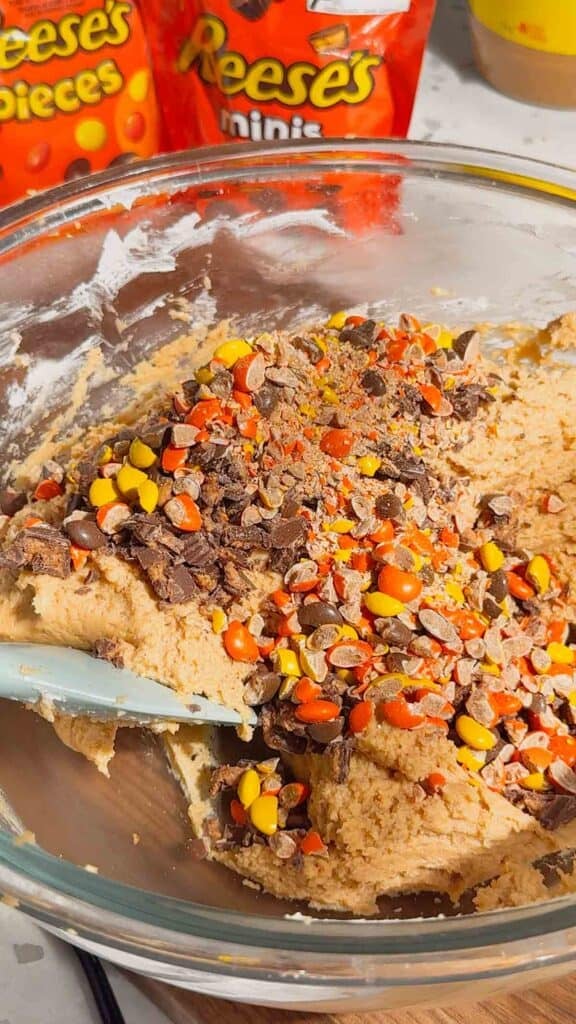 chopped reese's pieces and peanut butter cups on top of peanut butter cheesecake mixture in a mixing bowl