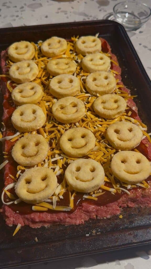 frozen smiley potatoes on top of meatloaf on a sheet pan