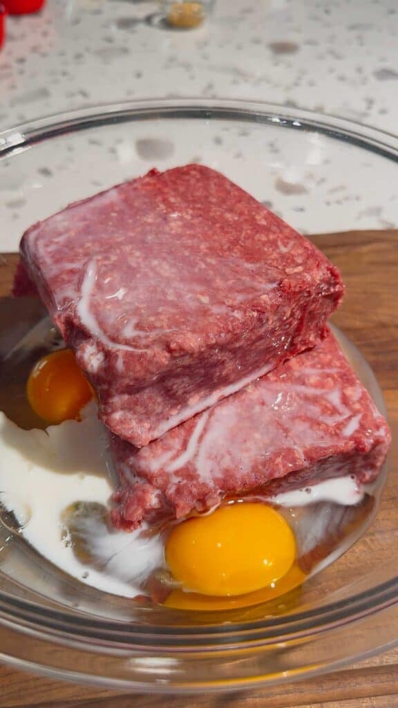 milk, eggs and raw ground beef in a glass mixing bowl