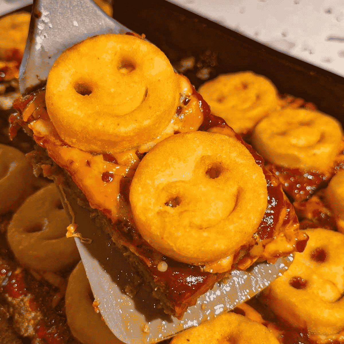 This Sheet Pan Meatloaf with Smiley Potatoes is an easy family dinner recipe loaded with seasoned ground beef, cheddar cheese, tangy ketchup BBQ sauce and crispy frozen smiley fries baked right on top. This kid friendly meatloaf recipe is perfect for busy weeknights, picky eaters, school night dinners and fun comfort food meals the whole family will love. Made with lean ground beef, bread crumbs, eggs, garlic, onions, shredded cheese and Sweet Baby Ray’s BBQ sauce, this sheet pan dinner is hearty, cheesy and simple to prep. Save this easy ground beef recipe for quick weeknight dinners, family meal ideas, meatloaf recipes, kid approved dinners, freezer potato recipes and fun dinner ideas for kids.