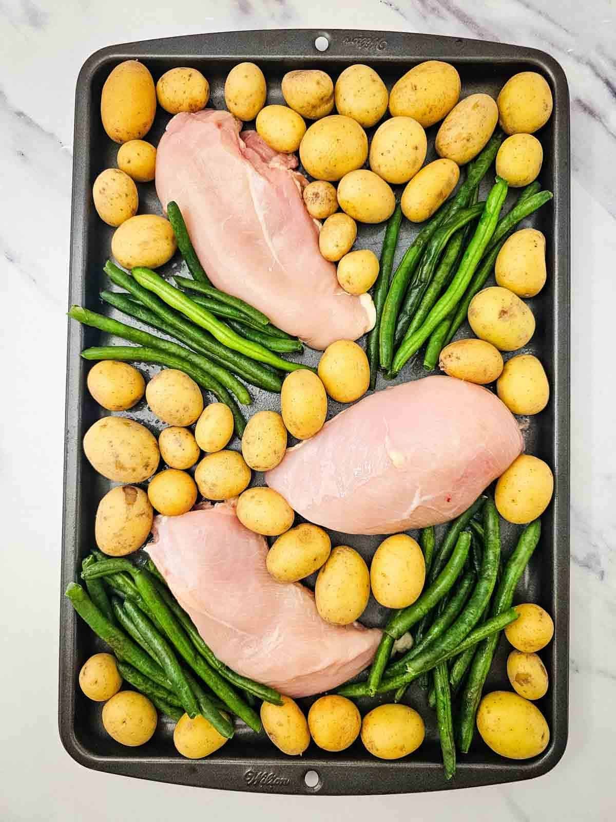 potatoes, green beans and raw chicken breasts on a sheet pan