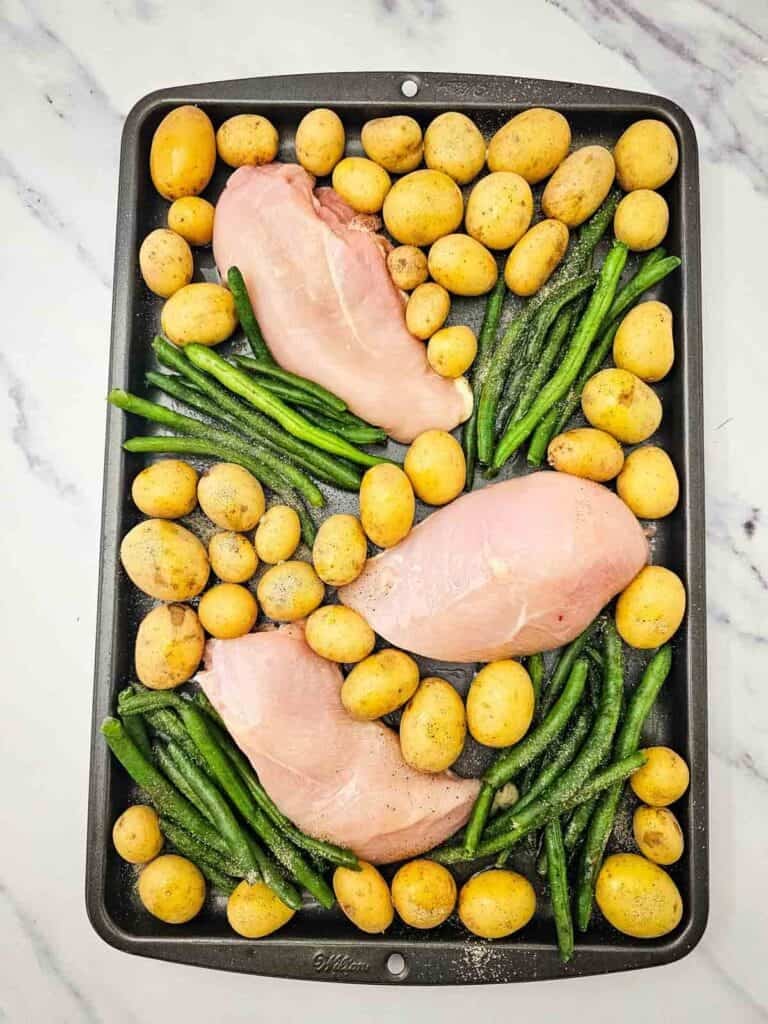green beans, potatoes and raw chicken breast on a baking sheet
