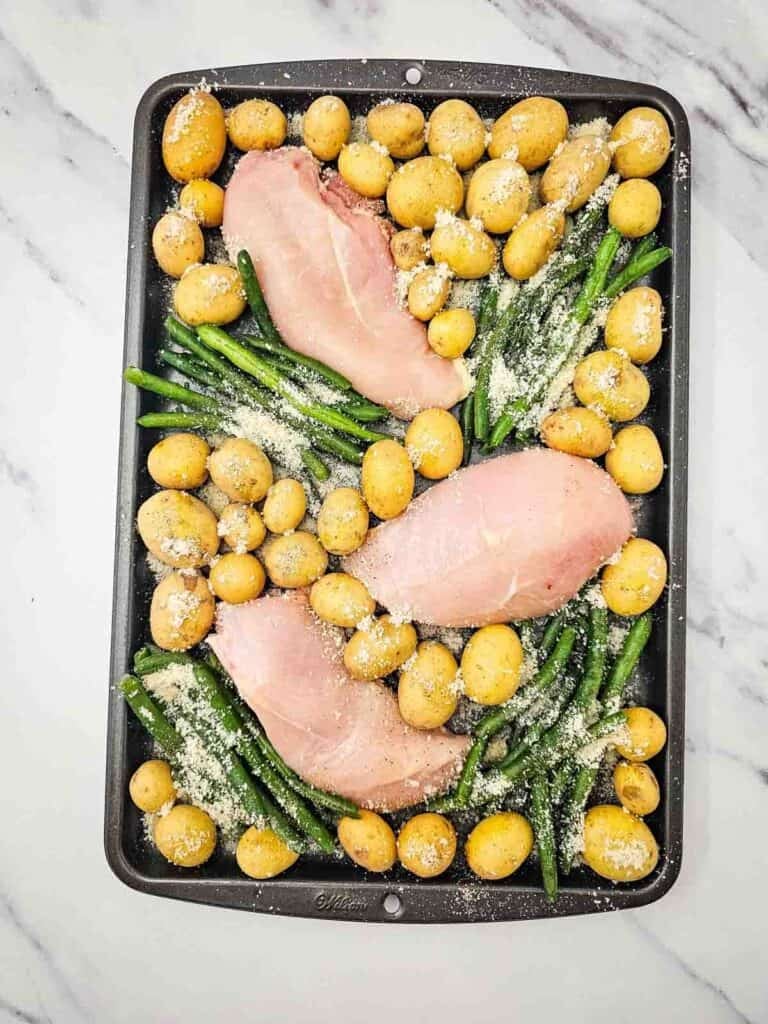 raw chicken breasts, green beans and baby potatoes on a sheet pan