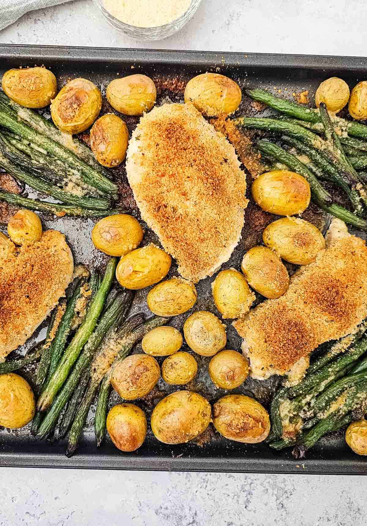 parmesan chicken on a baking sheet with green beans and baby potatoes