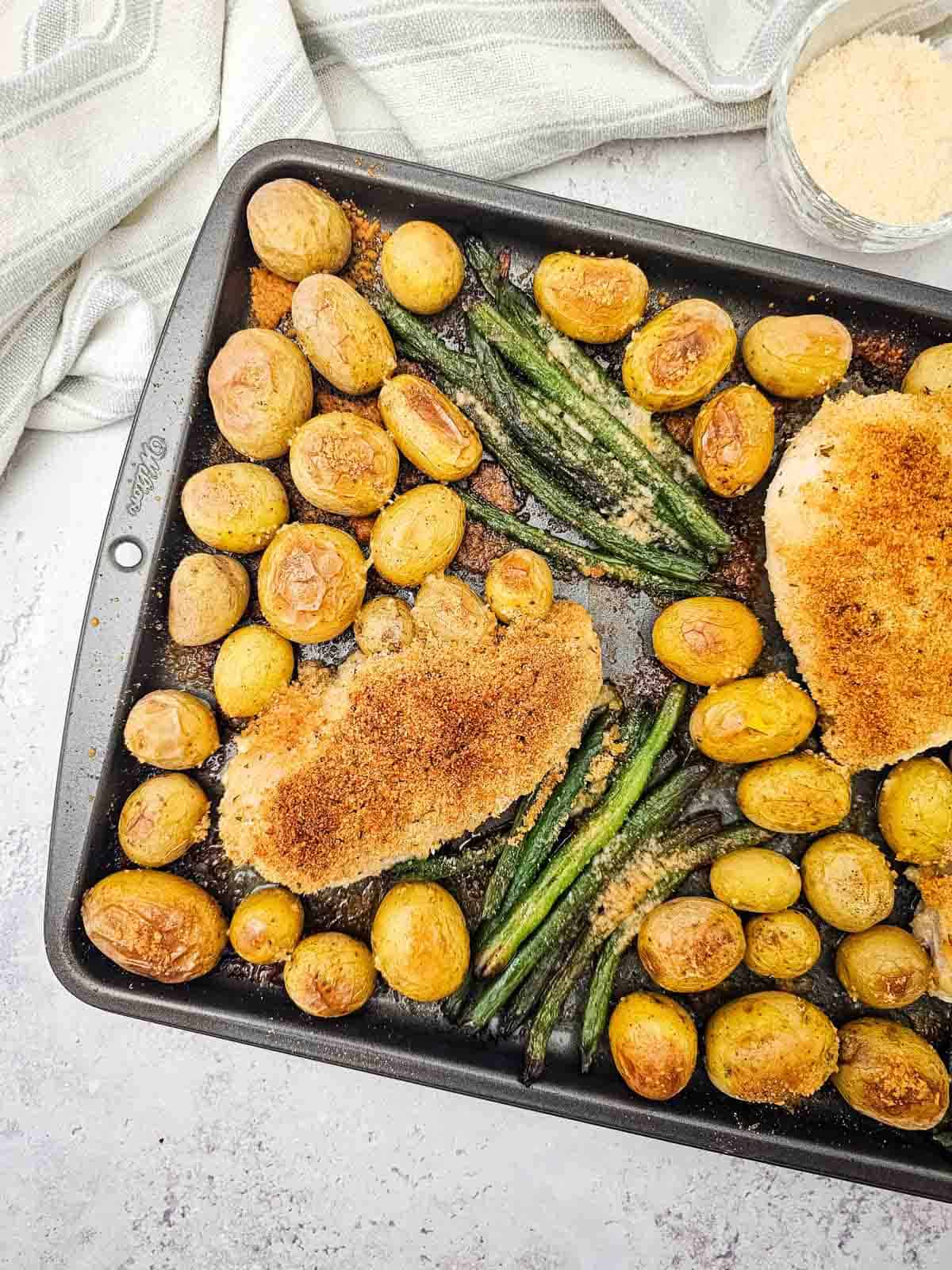 golden crusted chicken with green beans and potatoes on a baking sheet