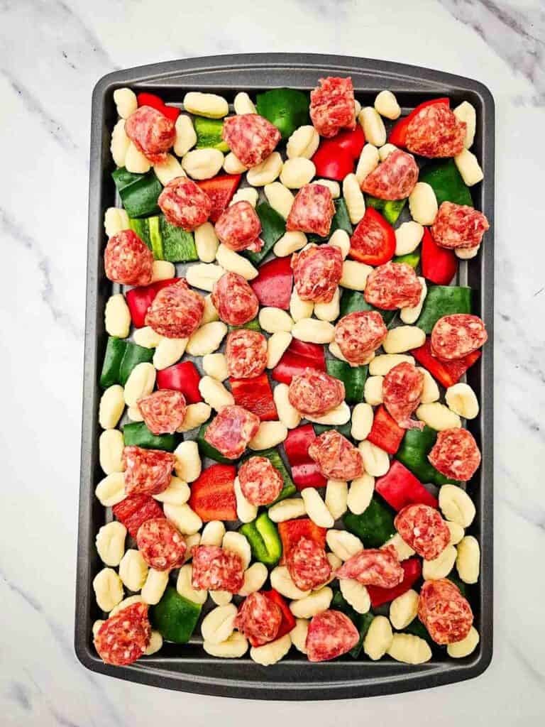 sliced sausage, gnocchi and bell peppers on a baking sheet