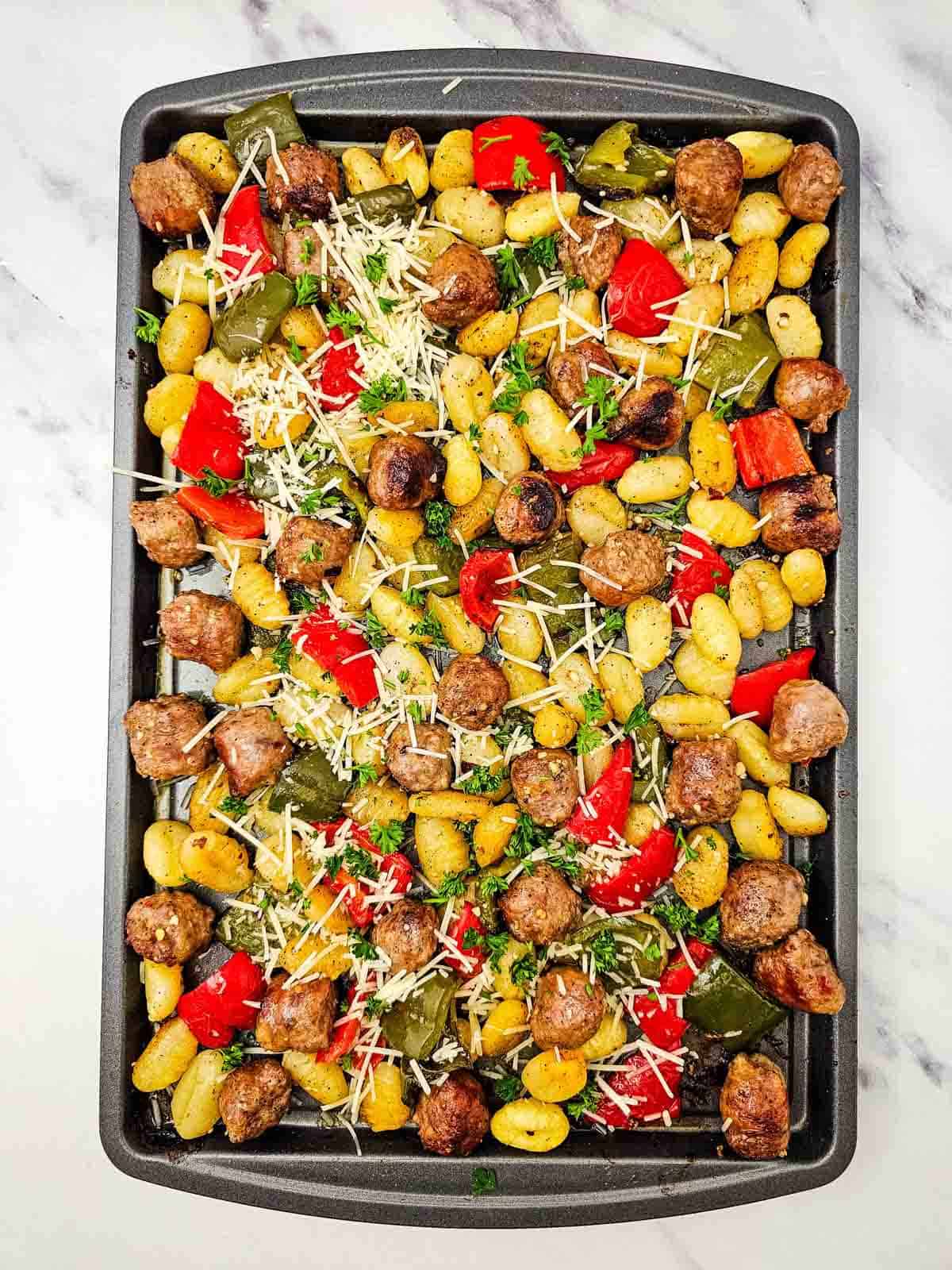 shredded parmesan sprinkled over sausage and gnocchi on a baking sheet