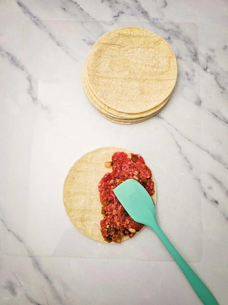 spreading taco meat mixture on a tortilla